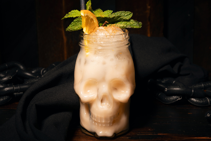 Cocktail drink with see-through skull shaped glass and mint and orange garnish