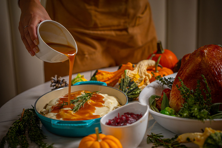 Potatoes with gravy pouring on top and cranberries and turkey with pumpkins on a table