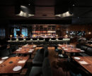 A dark-lit chic restaurant interior with an open kitchen.