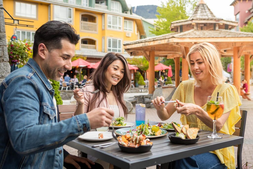 Three people dine happily outdoors in Whistler. 