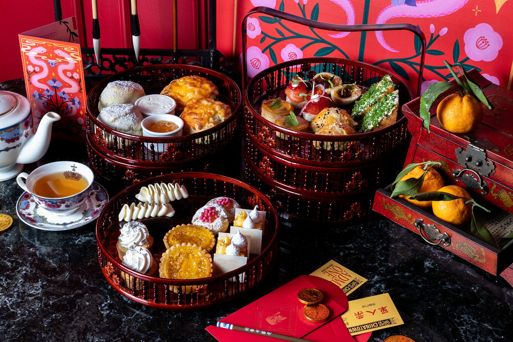 A tea service spread of brown trays featuring cakes, cookies, scones, and savoury bites. 