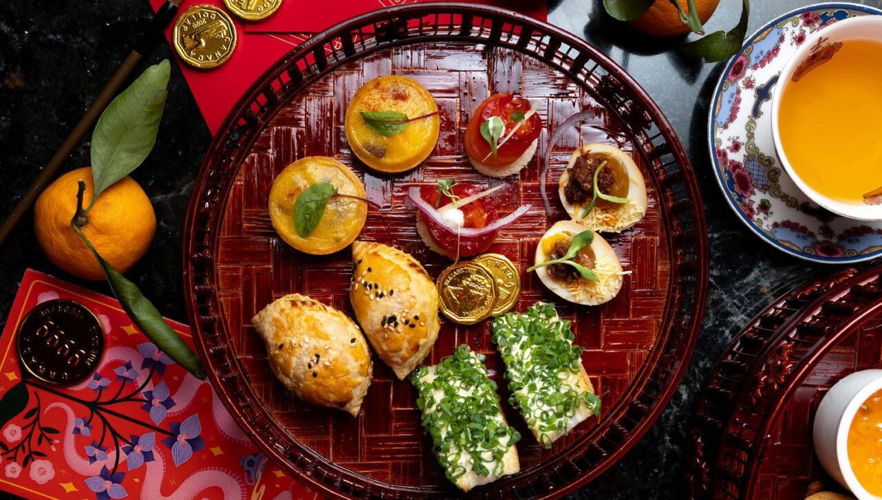 Afternoon tea tray spread with tarts, eggs, sandwiches, and more.