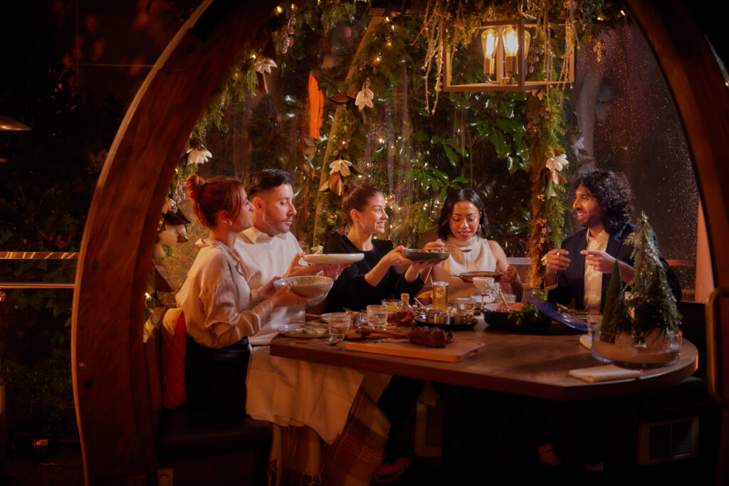 A group dines in a dome decorated with evergreens and seasonal holiday decor. 