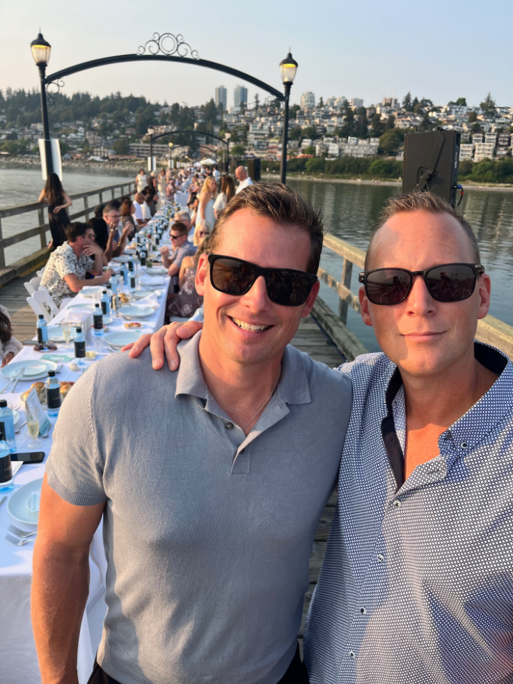 two men in polos smiling in front of a long table on the pier