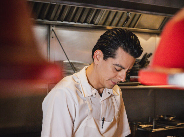 A dark haired chef prepares food in his white uniform.