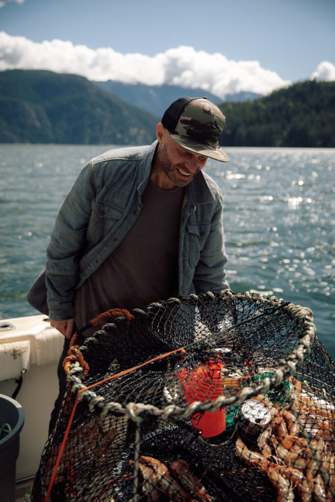 A man smiles looking at a full crab trap while on the deck of a boat on the ocean.