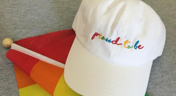 A white hat that says in rainbow coloured letters "Proud to be"