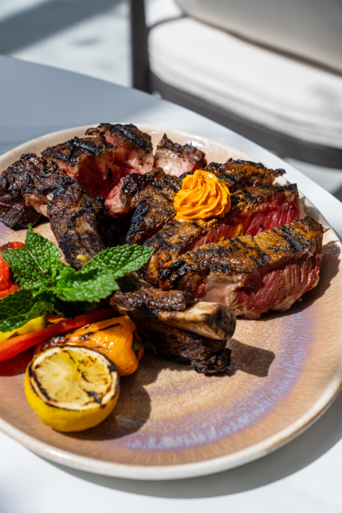 A large plate of sliced meat garnished with roasted lemon and fresh herbs. 