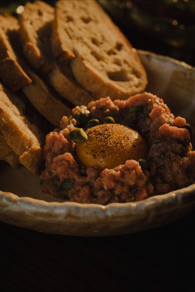 Egg yolk atop a beef tartare with toast. 