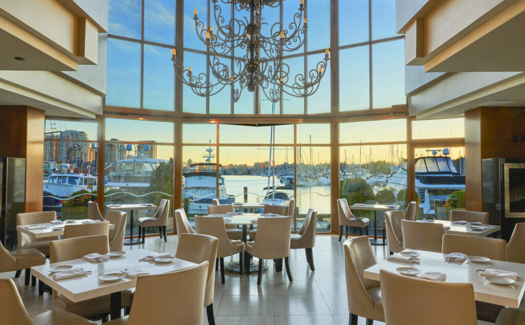 Floor to ceiling windows look out on a harbour view from a dining room. 