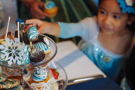 A girl in a blue princess dress reaches for some festive desserts. 