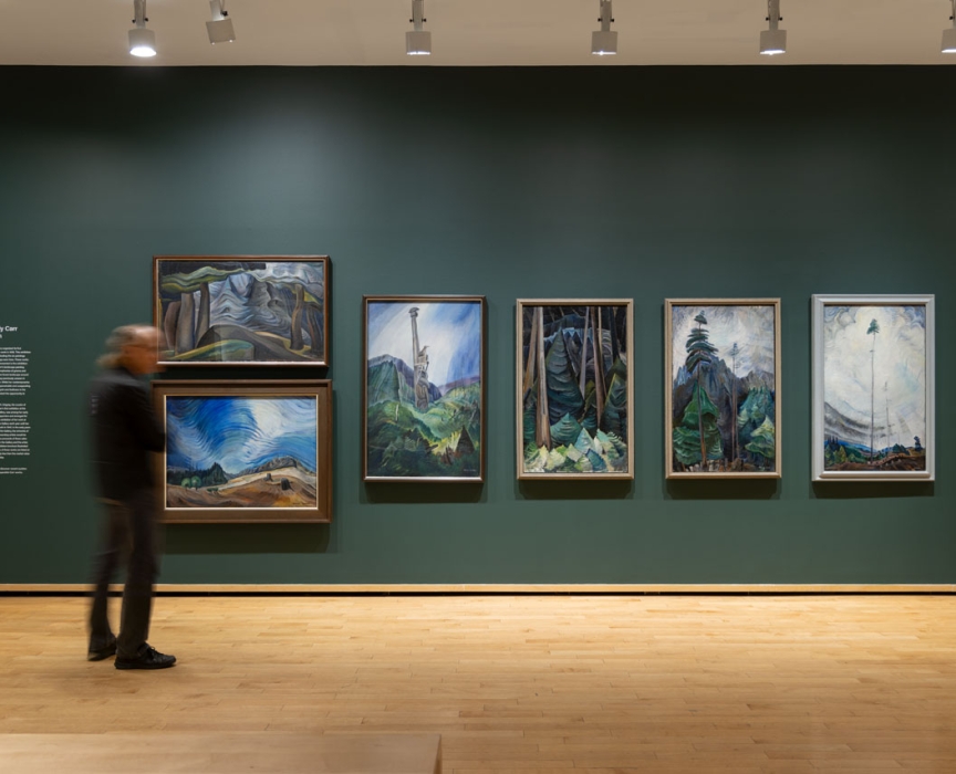 blurred figure standing in front of a row of Emily Carr paintings in Vancouver Art Gallery