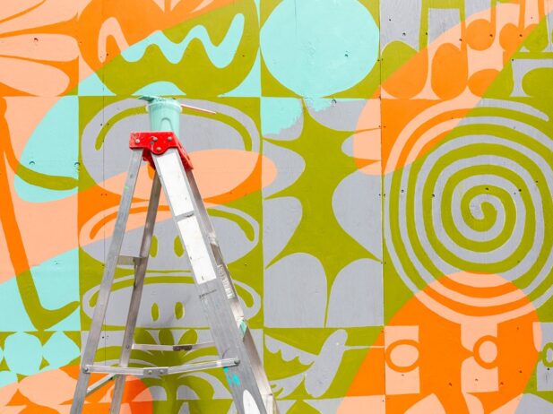A mural in the colors green, orange and blue with a ladder in front
