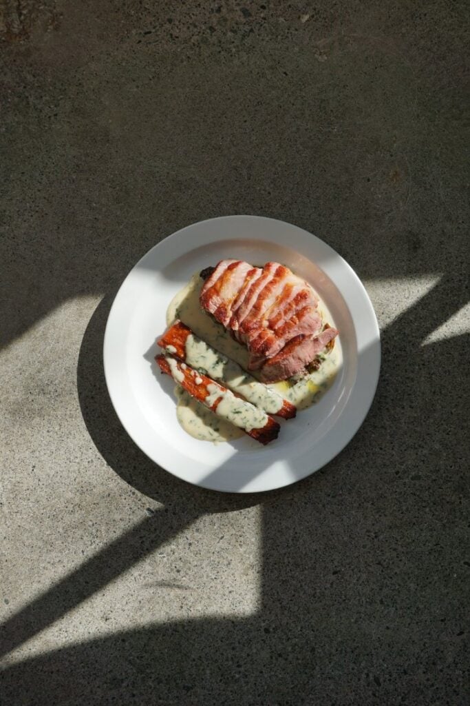 A white plate of sliced meat with a side of vegetables in the sunlight.