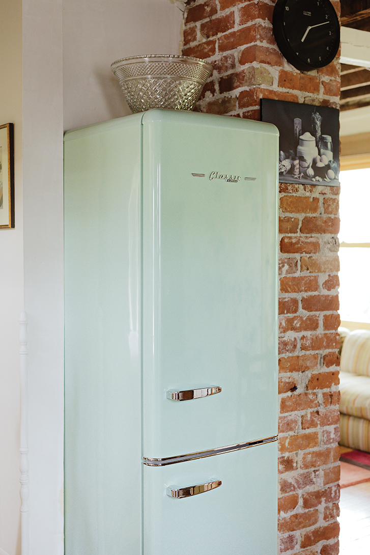 a slim, mint coloured fridge tucked next to a brick pillar