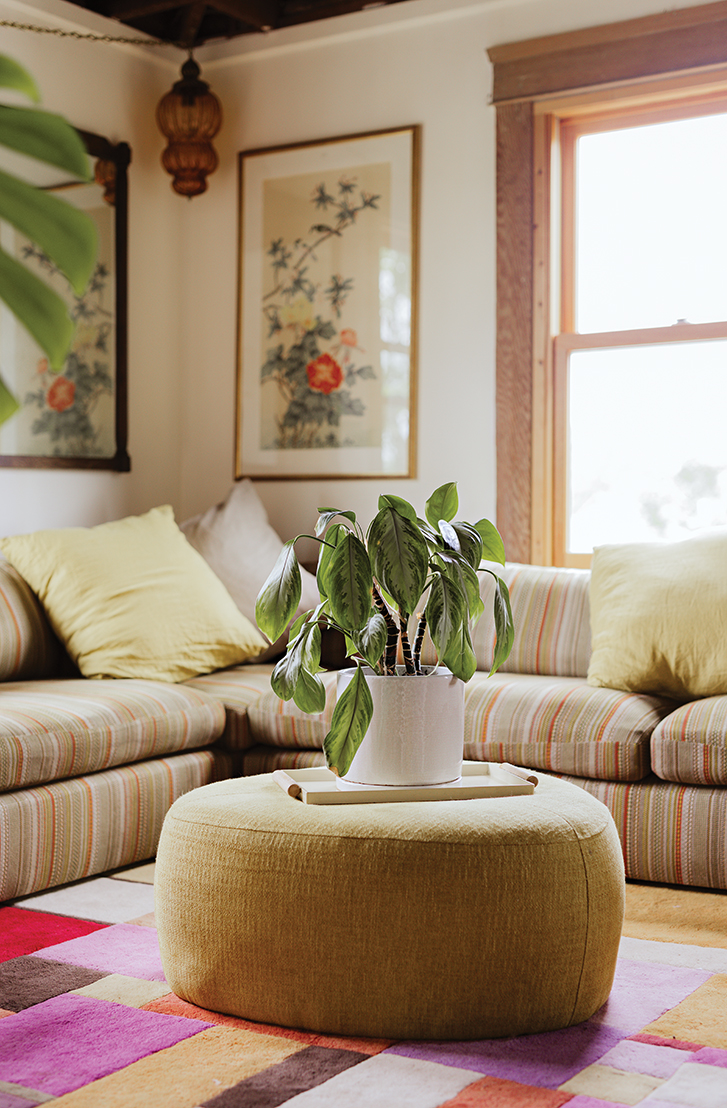 an L-shaped couch on a colourful, grid-patterned rug with a rounded ottoman at the centre