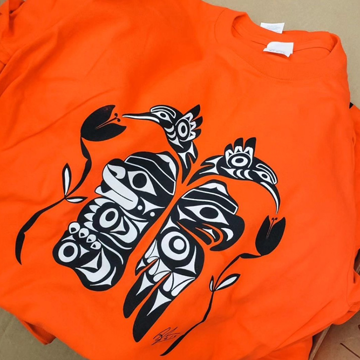Black and white design of a bear, an eagle, and two hummingbirds on an orange shirt.