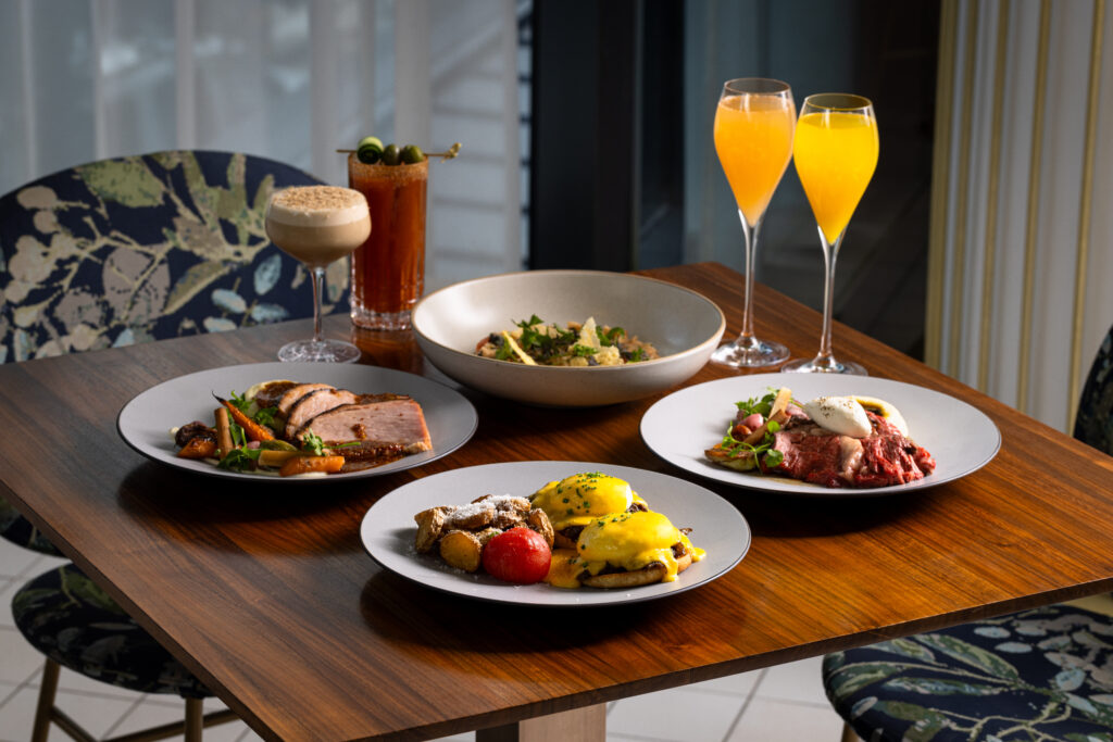 A wooden table set with mimosas and four heaping plates of brunch food.