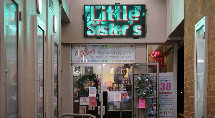 A picture of the entry of Little sisters bookstore on davie Street. With a glowing sign that says Little Sisters 