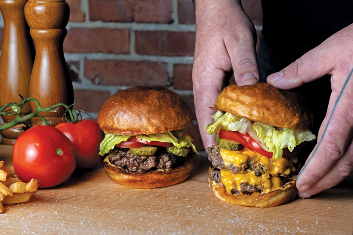 a pair of hands grabbing a burger from the counter at Monarch Burger