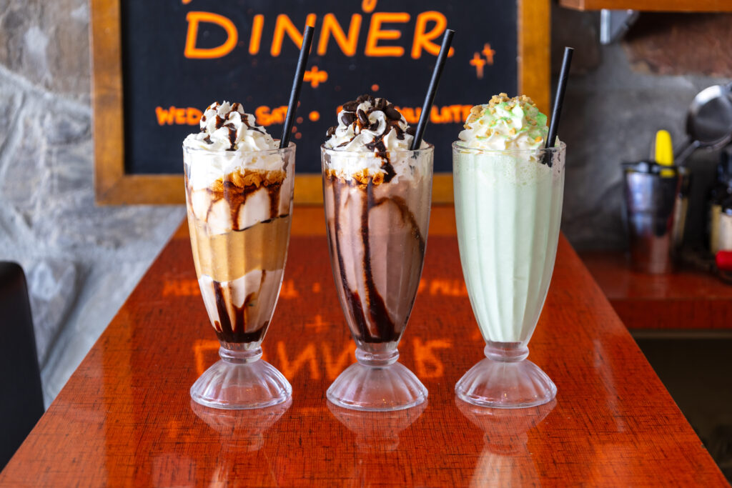 Three milkshakes topped with whipped cream on a red countertop. 