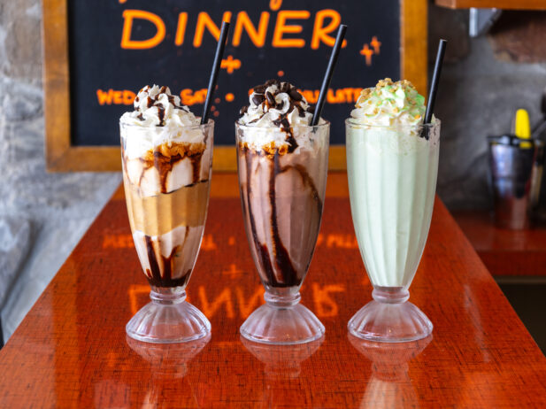 Three milkshakes topped with whipped cream on a red countertop.
