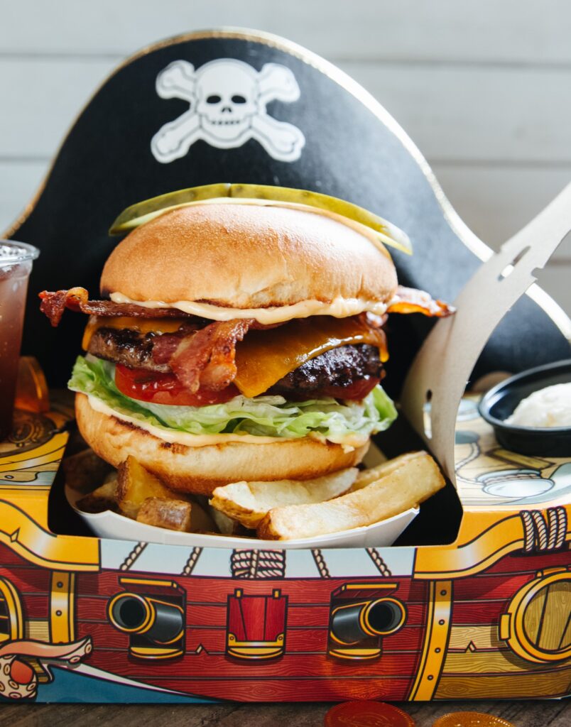 A big hamburger with fries in a pirate ship style pack.