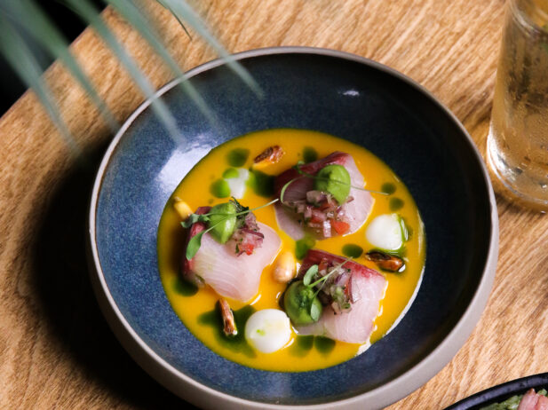 An artfully plated raw seafood dish atop a natural wood table.