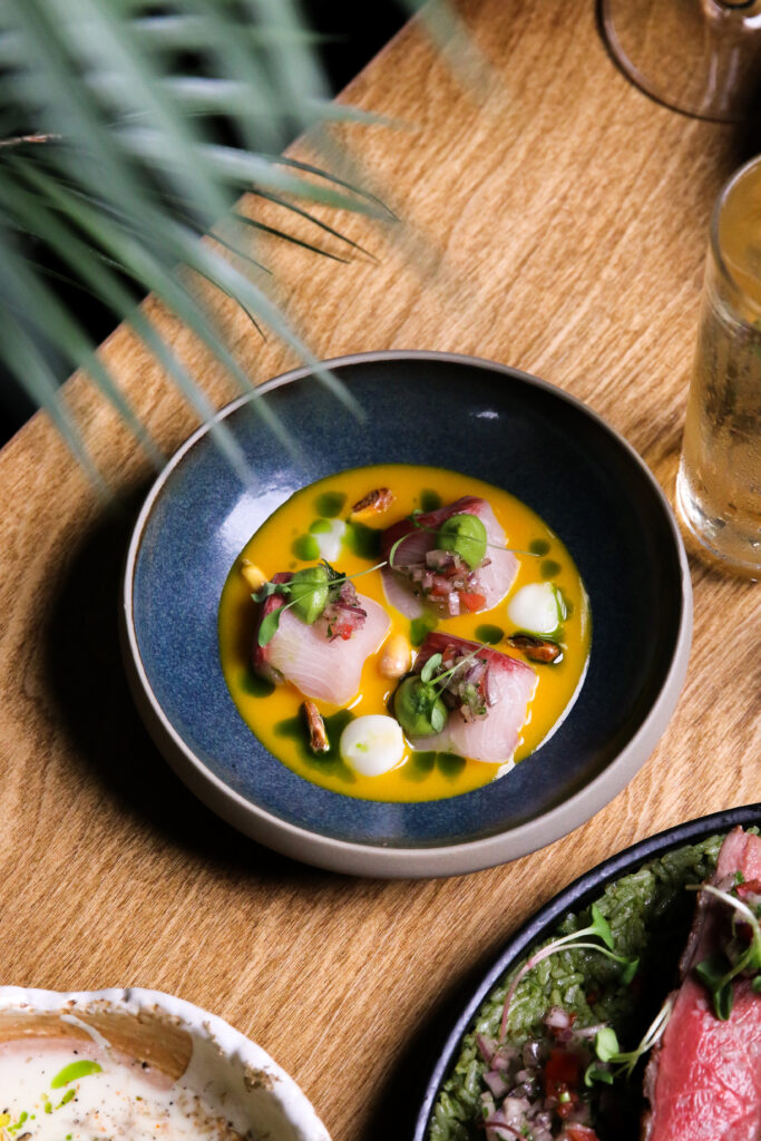 An artfully plated raw seafood dish atop a natural wood table. 