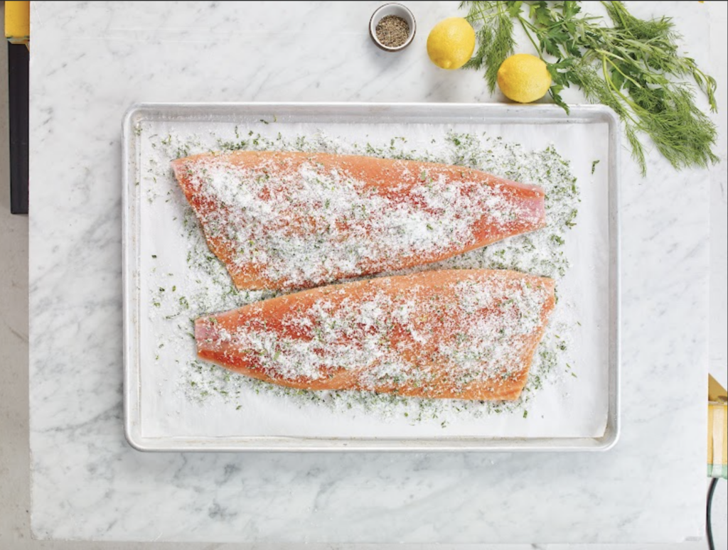 Salmon gravlax being prepared on a rectangular baking sheet.