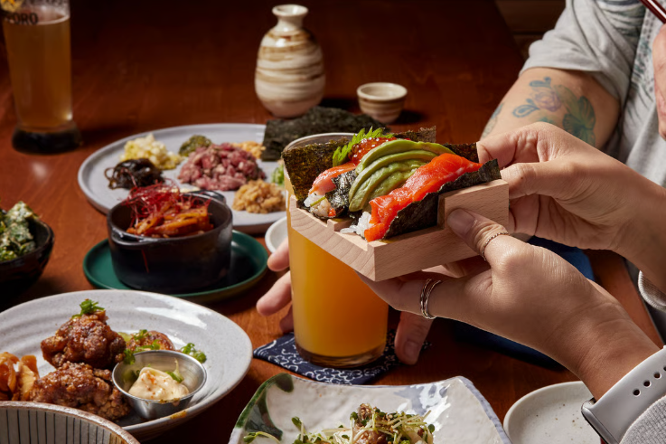 A table laden with sushi and hands serving it. 