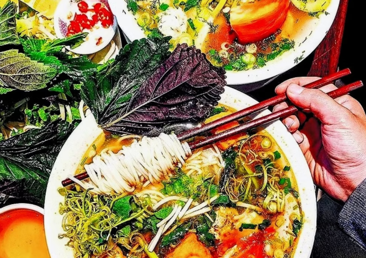 Chopsticks dip into noodle soup laden with vegetables and noodles. 