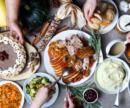 Full thanksgiving spread with turkey, mashed potatoes, pie, vegetables. Hands serving the dishes.