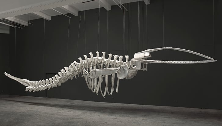Large, hanging sculpture of a whale skeleton made of plastic chairs.