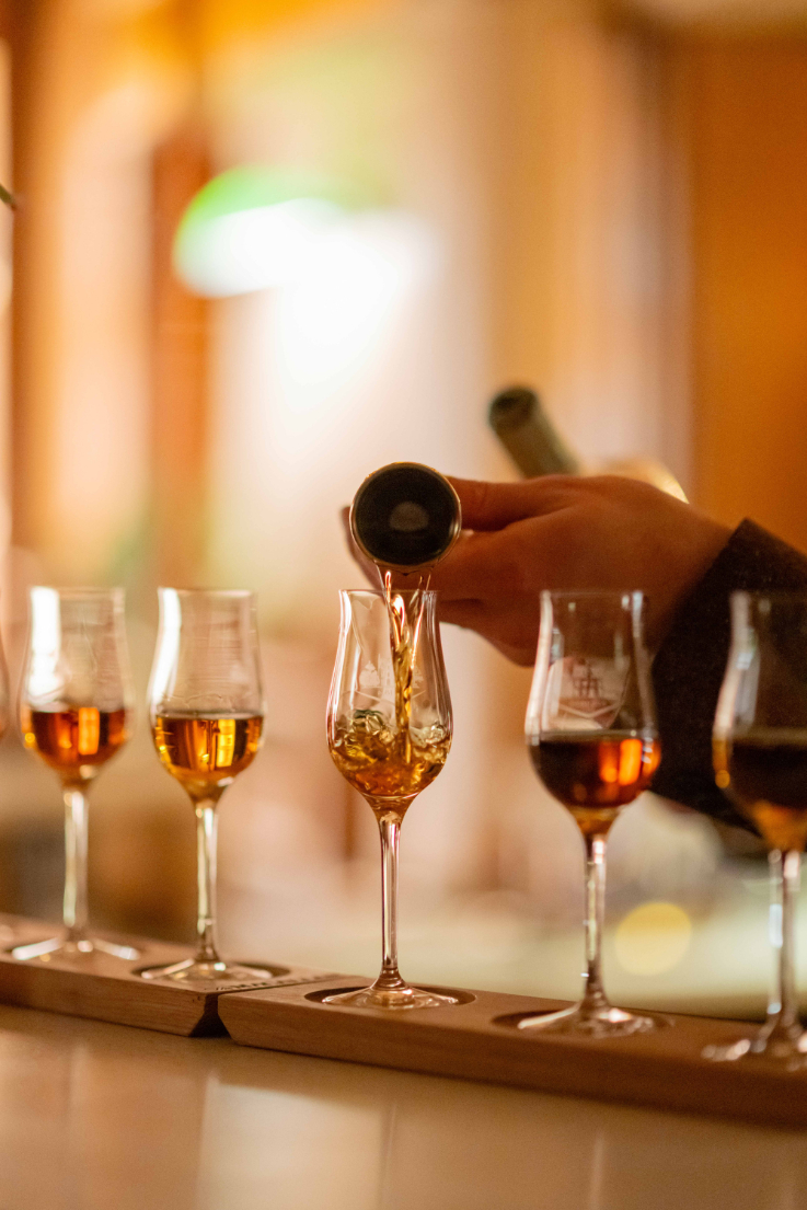 a hand pouring several tasting glasses of whisky