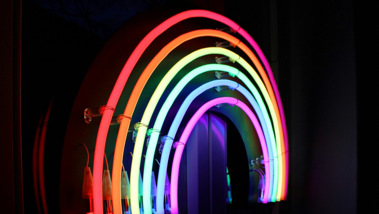 A rainbow made out of neon lights in front of a dark backdrop