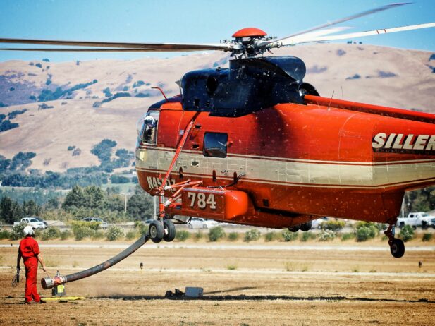 A fire-helicopter flying a low over the ground with a pilot next to it.