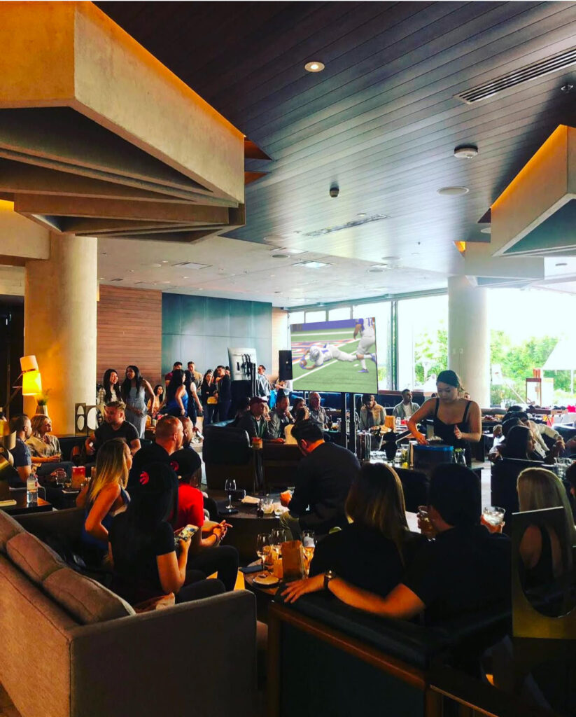 A crowd eating, drinking and watching a football game on a large screen. 