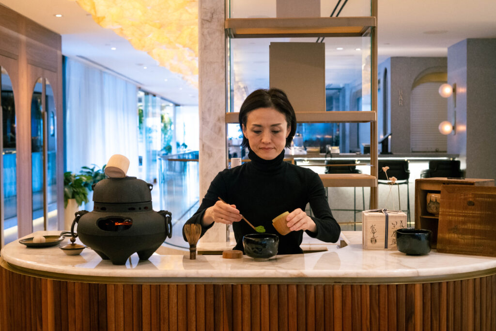 A woman in a black turtleneck spoons bright green matcha powder into a cup. 