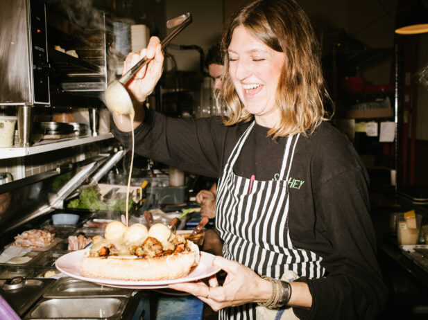 Chef in a striped apron ladles sauce over a meatball sandwich.