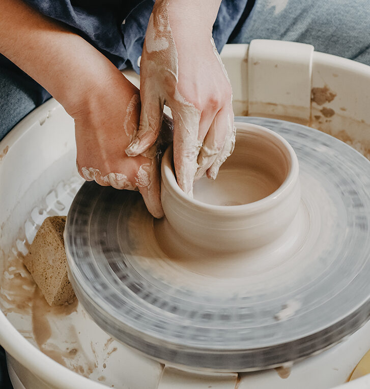 The female hands of a potter model a clay product on a wheel