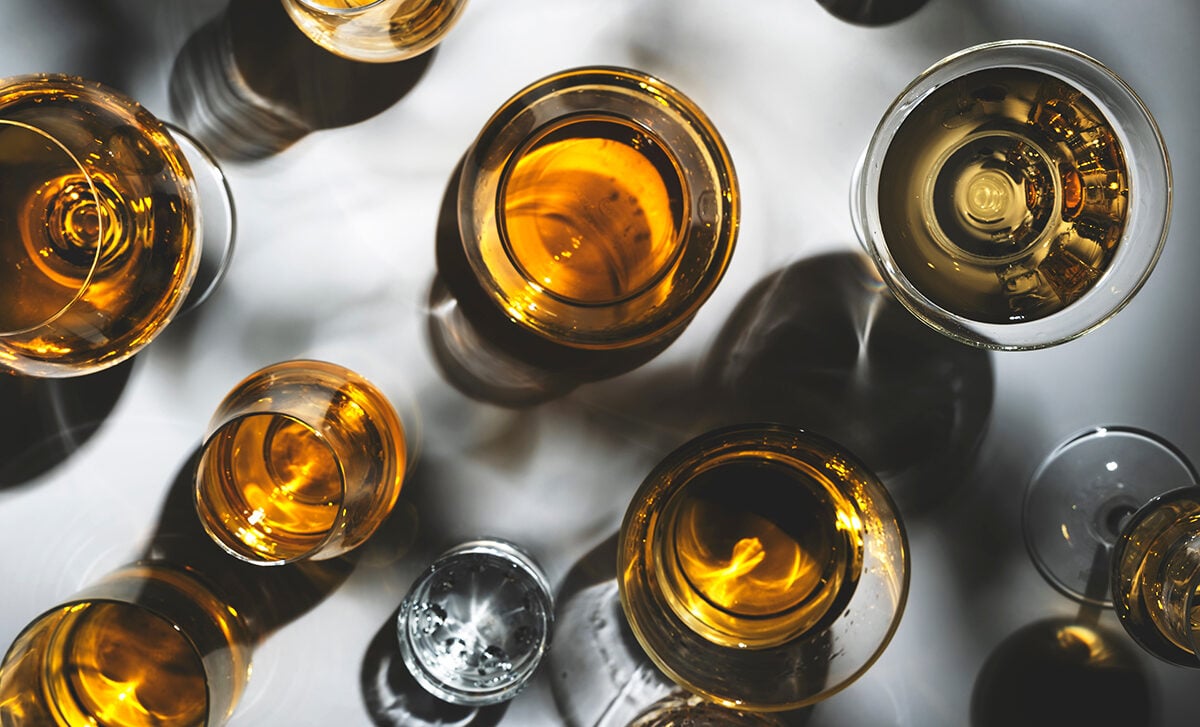 Hard strong alcoholic drinks, spirits and distillates in glasses: vodka, cognac, tequila, scotch, brandy and whiskey, grappa, vermouth, rum. White background with hard lights and shadows, top view